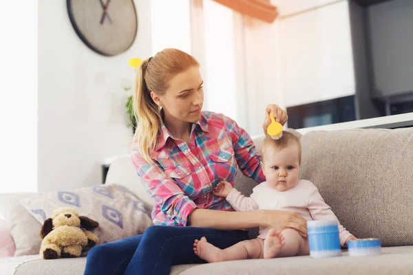 Een vrouw is zittend op de Bank en kammen van haar baby. Het kind houdt te kammen. — Stockfoto