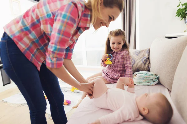 En kvinna swaddling ett litet barn på soffan. Bredvid henne den äldsta dottern till en kvinna som tittar på process. — Stockfoto