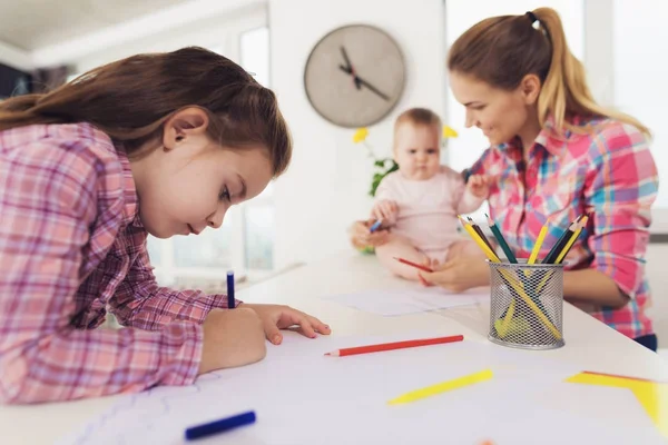 Une petite fille dessine sur le dessus de la cuisine avec des crayons de couleur. La mère d'une fille avec un bébé est assise côte à côte . — Photo