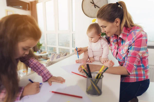 Маленькая девочка рисует на кухонном верху цветными карандашами. Мать девочки с ребенком сидит бок о бок . — стоковое фото