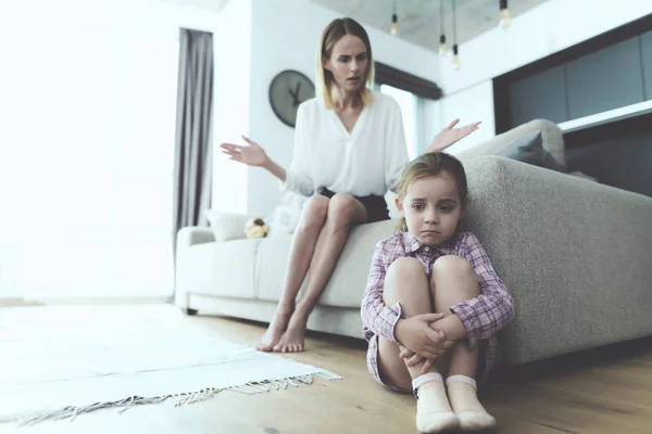 La femme parle à une petite fille offensée, assise à côté du canapé, les jambes baissées. . — Photo