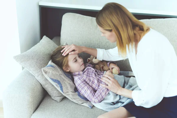 Una donna è seduta accanto a una bambina malata. E 'sdraiata sul divano ed è malata. . — Foto Stock