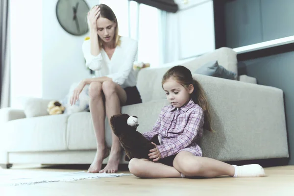 Жінка розмовляє з маленькою ображеною дівчинкою, яка сидить поруч з диваном і тримає в руках іграшку . — стокове фото