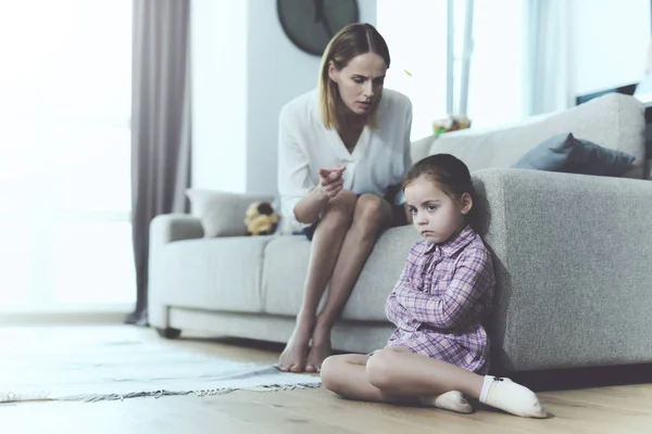 Женщина разговаривает с маленькой, обиженной девочкой, которая сидит рядом с диваном с заправленными ногами . — стоковое фото