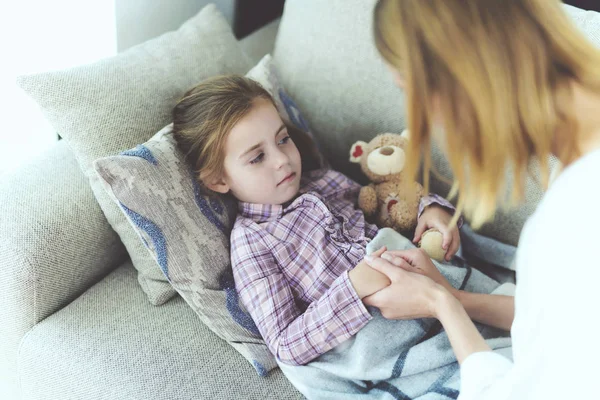 Una donna è seduta accanto a una bambina malata. E 'sdraiata sul divano ed è malata. . — Foto Stock