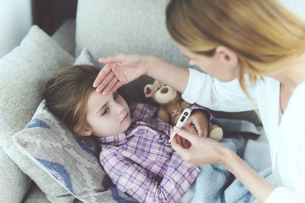 Жінка сидить поруч з маленькою дівчинкою, яка хворіє. Вона тримає термометр, який виміряла температура дівчини . — стокове фото