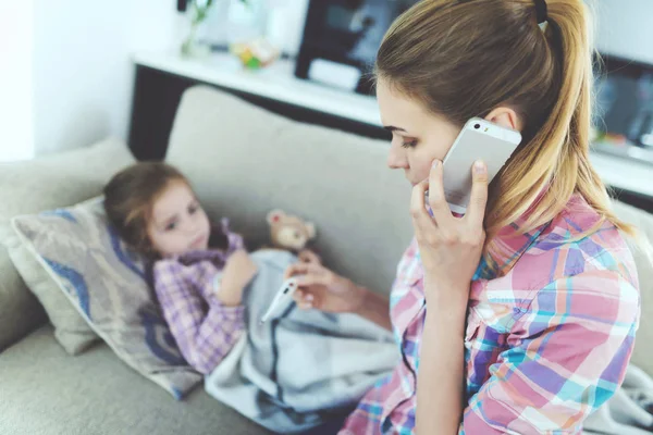 A woman is sitting next to a little girl who is sick. She holds a thermometer, which the girl's temperature measured. — Stock Photo, Image