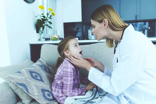 Küçük kız hastalandı. Bir doktor ona geldi ve boğazını muayene. — Stok fotoğraf