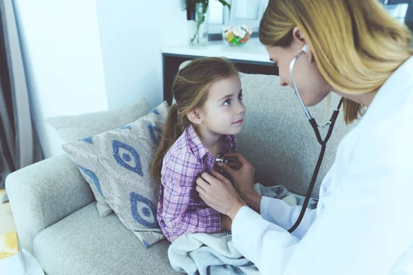 La niña cayó enferma, un médico se acercó a ella y la escuchó con un estetoscopio. . —  Fotos de Stock