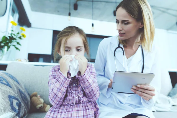 La niña se enfermó y un médico vino a verla. La chica se sonó la nariz en una servilleta. El médico llena el formulario . —  Fotos de Stock