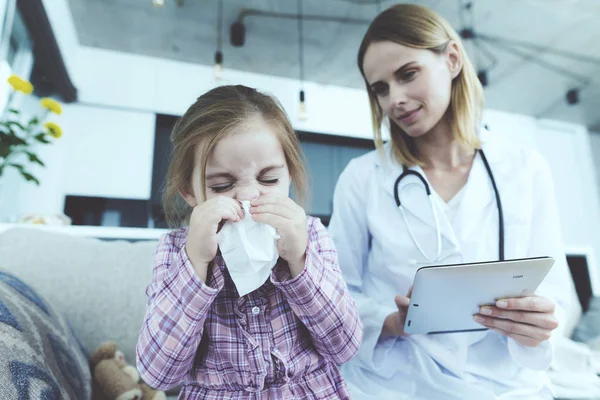 La niña se enfermó y un médico vino a verla. La chica se sonó la nariz en una servilleta. El médico llena el formulario . —  Fotos de Stock