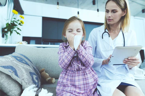 La niña se enfermó y un médico vino a verla. La chica se sonó la nariz en una servilleta. El médico llena el formulario . —  Fotos de Stock