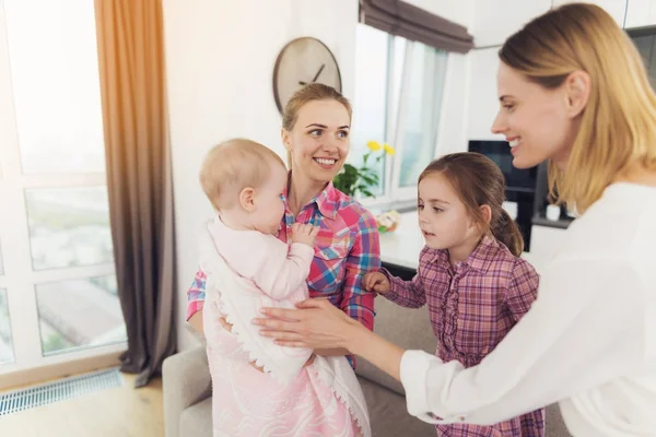 The babysitter meets the mother of the children, holding the baby in her arms. The older girl hugs Mom. — Stock Photo, Image