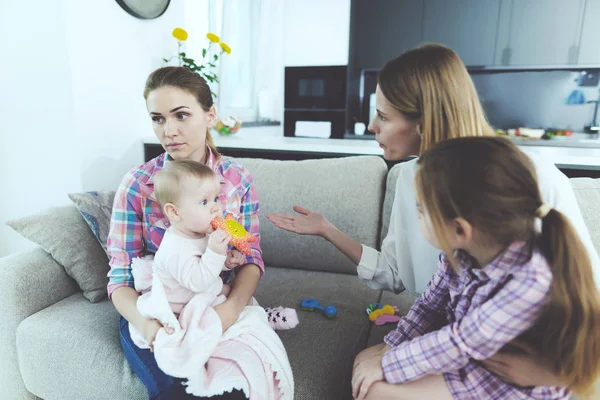Babysitter parlare con la madre dei bambini. Tiene il bambino tra le braccia. La madre dei bambini rimprovera l'infermiera . — Foto Stock