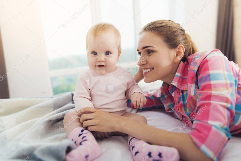 A woman is lying on the bed next to the baby. She will put the baby to bed.
