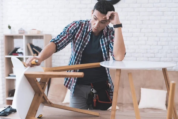 Mladý muž se snaží sám složit svůj stolek a židle. — Stock fotografie