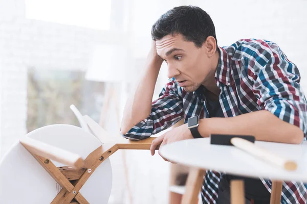 Le jeune homme essaie de plier sa table basse et ses tabourets . — Photo