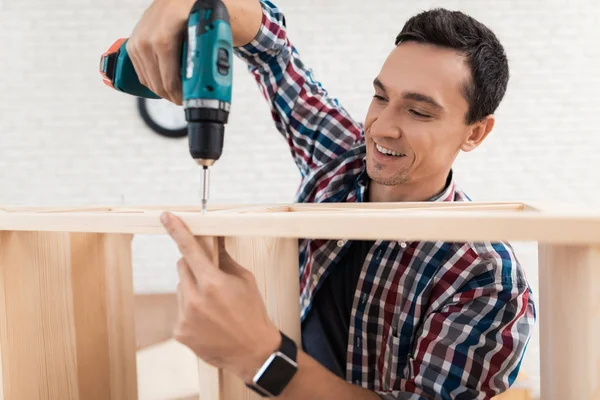 The young man tries himself to fold his bookcase. — Stock Photo, Image