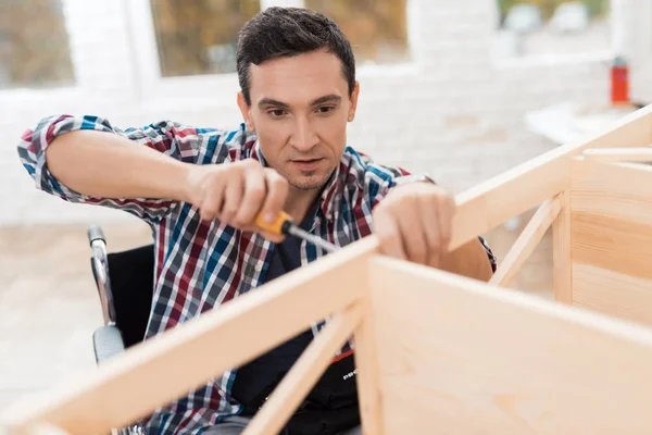 The young man in wheelchair tries himself to fold his bookcase. — Stock Photo, Image