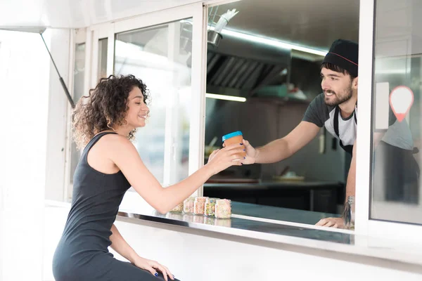 Una hermosa chica en un vestido negro se acercó al camión de comida. Pidió café para ella. El vendedor se lo da. —  Fotos de Stock