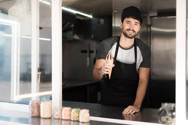 Un hombre en un delantal posando en un restaurante móvil. Está sosteniendo un delicioso helado de chocolate —  Fotos de Stock