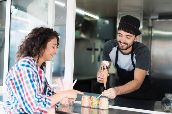 A beautiful girl in a plaid shirt ordered chocolate ice cream. A man in a mobile diner gives her ice cream