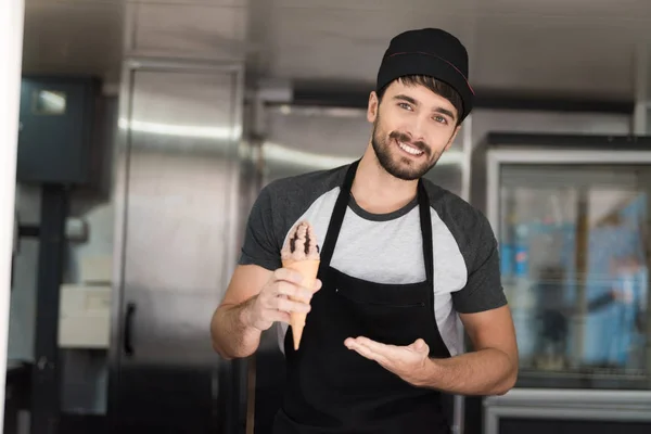 Un hombre en un delantal posando en un restaurante móvil. Está sosteniendo un delicioso helado de chocolate —  Fotos de Stock