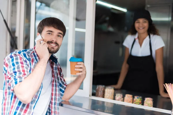 격자 무늬 셔츠에 남자가 음식 트럭에 갔다. 그는 자신을 위해 커피를 주문. 그것은 아름 다운 소녀 판매자에 의해 제공 됩니다. — 스톡 사진