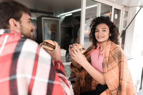 Una joven pareja está parada junto a un bar móvil en la calle. Pidieron dos jugosas y fragantes hamburguesas. —  Fotos de Stock