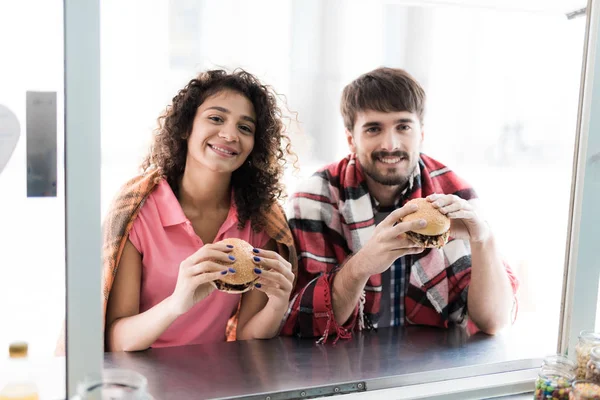 Una joven pareja está parada junto a un bar móvil en la calle. Pidieron dos jugosas y fragantes hamburguesas. —  Fotos de Stock