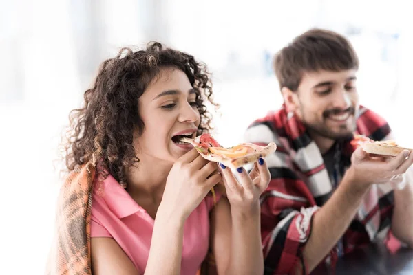 A young couple is standing by a mobile snack bar in the street. They ordered two pieces of tasty pizza and eat it — Stock Photo, Image