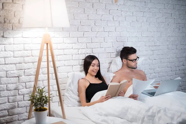 Un tipo está acostado en la cama y trabajando en un portátil. El tipo no presta atención a su novia . —  Fotos de Stock