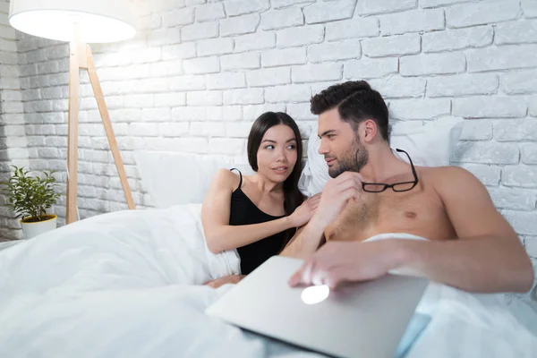 Ein Kerl liegt im Bett und arbeitet an einem Laptop. das Mädchen liegt auf der Brust des Mannes. — Stockfoto