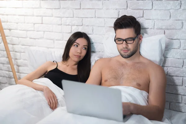Facet jest leżenie w łóżku i pracy na laptopie. Dziewczyna leży na piersi mężczyzny. — Zdjęcie stockowe