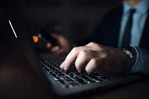Un uomo e 'seduto davanti a un portatile in un ufficio buio. L'uomo vestito lavora fino a tardi. . — Foto Stock