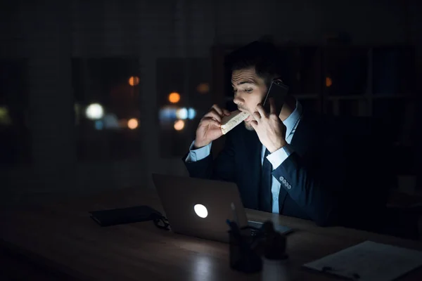 Ένας άνδρας κάθεται σε ένα φορητό υπολογιστή σε ένα γραφείο σκούρο. Ο άνθρωπος στο κοστούμι που λειτουργεί μέχρι αργά το βράδυ. — Φωτογραφία Αρχείου