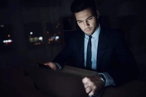 Un hombre está sentado en una laptop en una oficina oscura. El hombre del traje trabaja hasta tarde. . —  Fotos de Stock