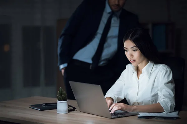 Fille et homme travaillent tard dans le bureau sombre. Jeune belle fille et femme d'affaires dans le bureau . — Photo