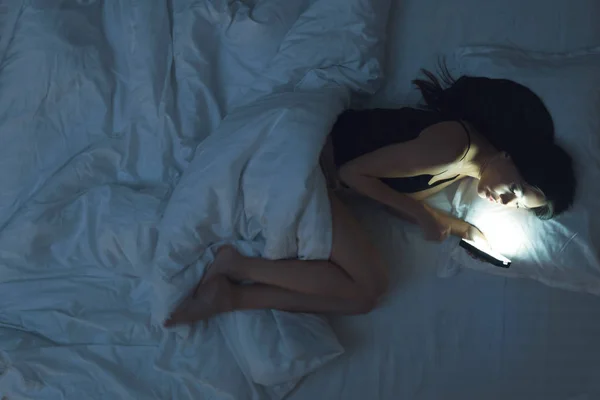 Girl is lying on the bed in underwear and looks into smartphone. Social networks and loneliness.