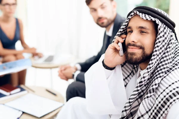 An arab businessman talks on the phone while discussing a business deal with his business partners. — Stock Photo, Image
