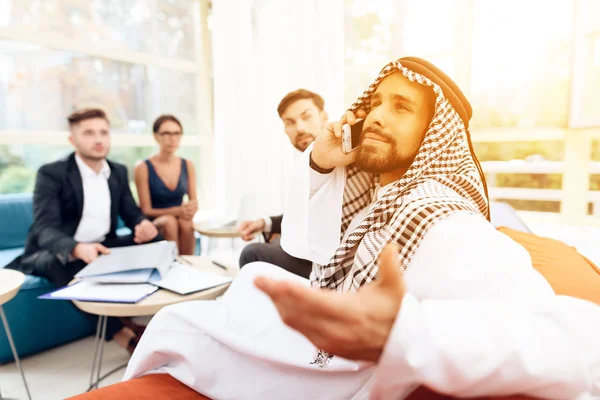 Een Arabische zakenman gesprekken over de telefoon tijdens de bespreking van een zakelijke deal met zijn zakelijke partners. — Stockfoto