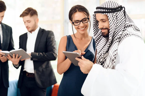 A girl shows something to a man in arabic clothes on a tablet. — Stock Photo, Image