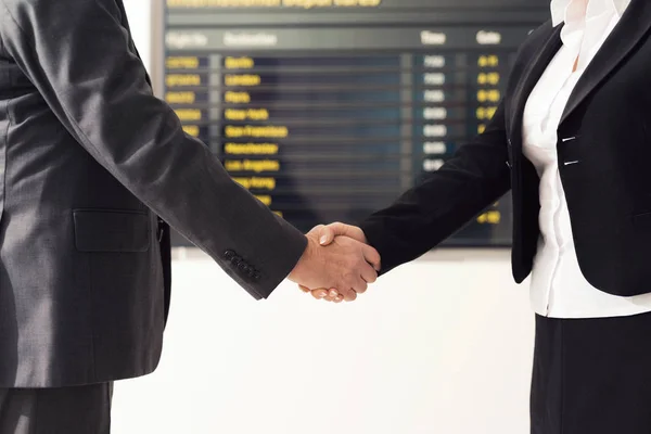 Επιχειρηματική συνάντηση στην αίθουσα του αεροδρομίου. Ένας άνθρωπος με μια γυναίκα τινάζει τα χέρια κοντά το χρονοδιάγραμμα. — Φωτογραφία Αρχείου