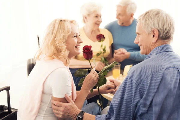 Un anciano da rosas a una anciana. Están sentados en el sofá. . — Foto de Stock