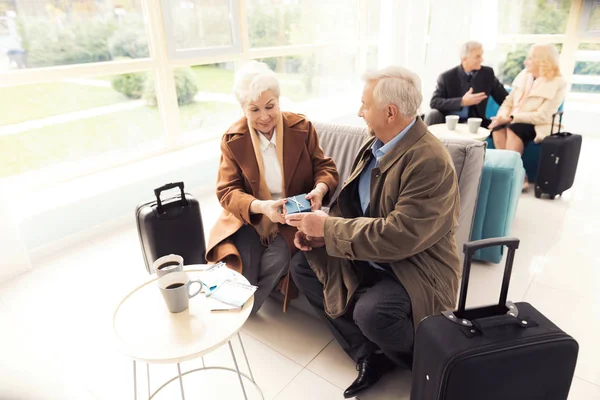 Elderly couple in the airport lounge. An elderly man makes an unexpected gift to an elderly woman.