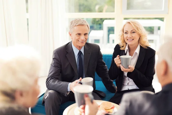 Un anciano y una anciana de traje. Beben café en la sala de espera. Reunión de negocios en el aeropuerto — Foto de Stock