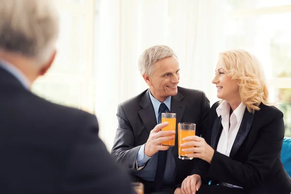 Una anciana y un anciano con trajes sostienen vasos con jugo de naranja . — Foto de Stock