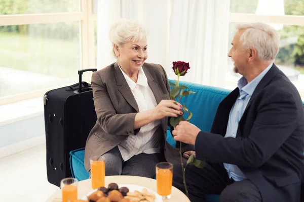 老人は、高齢者の女性にバラを与えます。彼らはソファの上に座っています。. — ストック写真