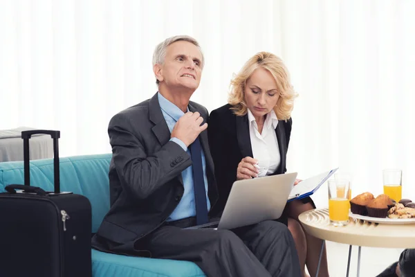 Business meeting in the airport hall. An elderly woman and an elderly man are sitting on the couch. — Stock Photo, Image