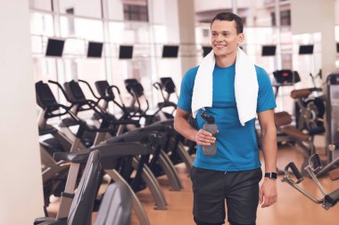 Genç bir adam spor salonunda poz. Kaslı adam mavi T-shirt gülümsüyor.